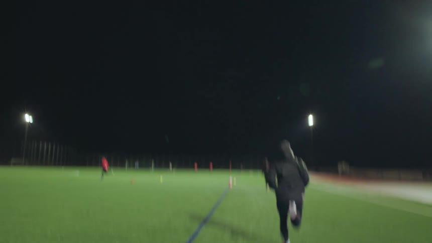A follow shot of an athlete sprinting across a brightly lit soccer field during a nighttime training session