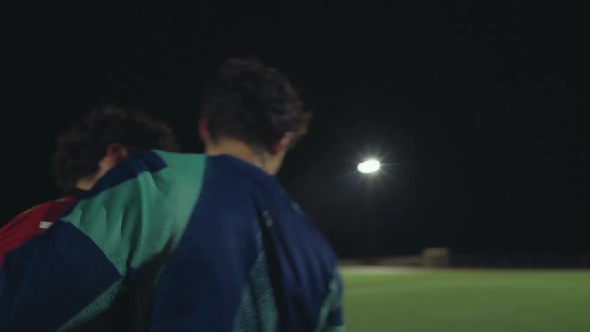 Two young male soccer players show sportsmanship, shaking hands and walking off the field arm-in-arm at night in slow motion
