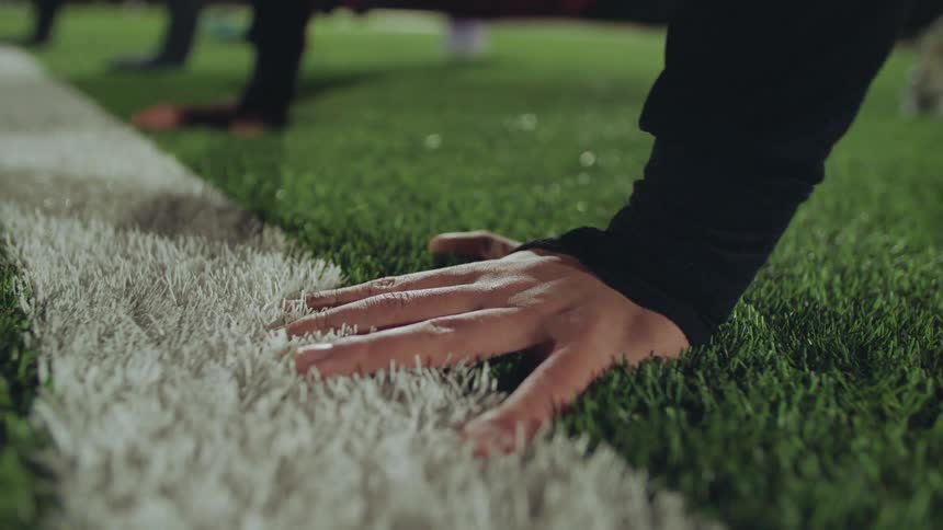 A close-up of an athlete's hand on the white line of an artificial turf field while doing push-ups during a night training session