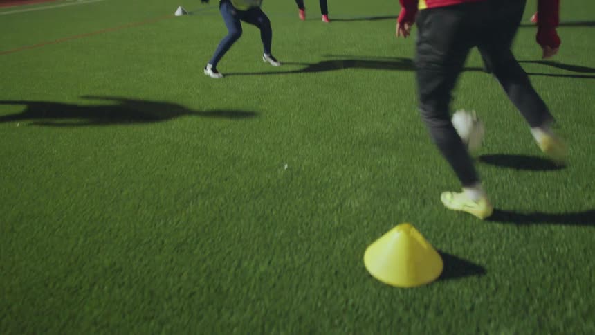 A slow-motion close-up of soccer players' feet as they participate in footwork and passing drills on an artificial turf field at night