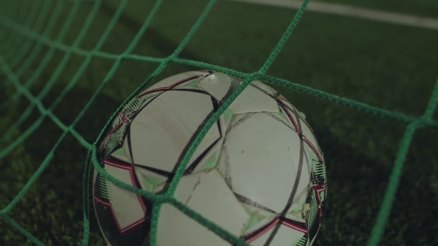 A close-up view of a soccer ball resting inside the goal net on a green turf field
