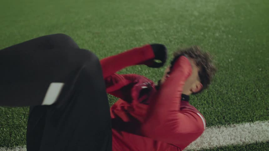 A determined young male athlete performs crunches on an artificial turf field at night