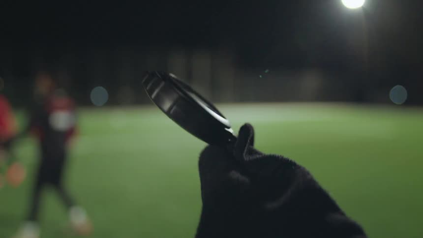 POV of a coach holding a stopwatch and timing athletes during a soccer practice on a green field at night