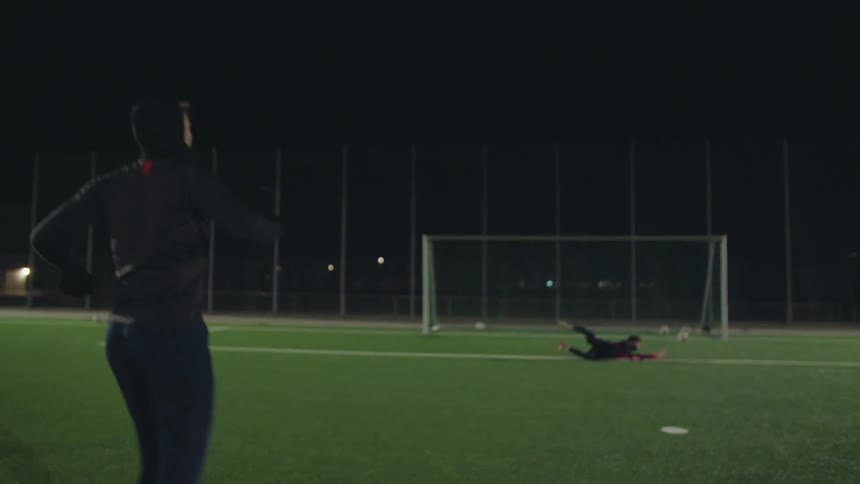 A soccer player kicks a powerful penalty shot at the goalie during a night practice in slow motion