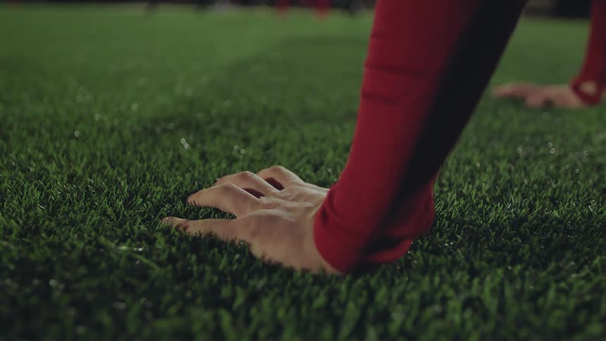 Close up of an athlete's hand pressing into the artificial turf as they do push-ups on a sports field at night