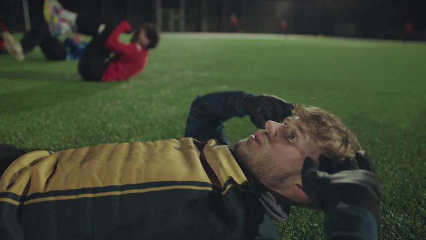 Close up slow motion of an exhausted male athlete doing sit-ups during a late night training session on a soccer field