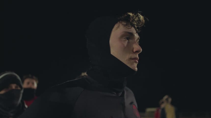 Intense profile shot of a young athlete wearing a black balaclava, concentrating on the field during a nighttime practice