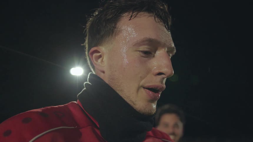 An exhausted soccer player in a red jersey catches his breath as steam visibly rises from his mouth on a cold night
