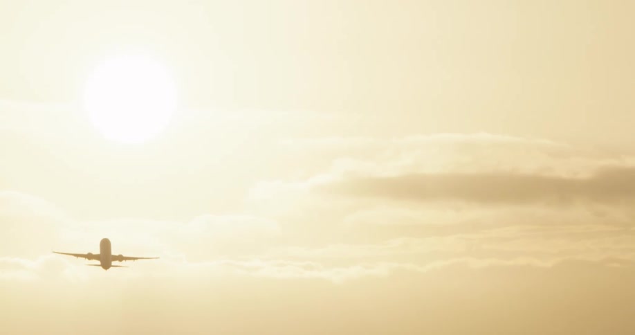 A silhouetted passenger jet takes off and flies into the bright golden sun in a hazy sky
