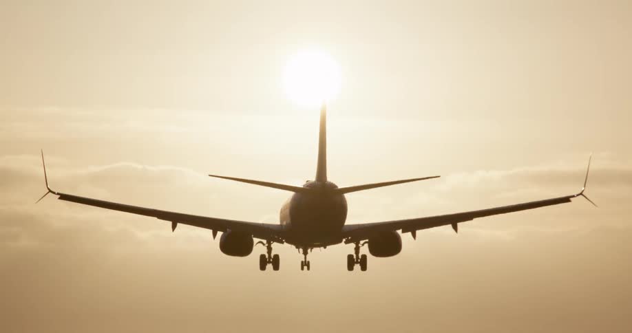 In a stunning slow-motion shot, a passenger airplane descends from a golden sky and lands directly on the runway, silhouetted by the sun