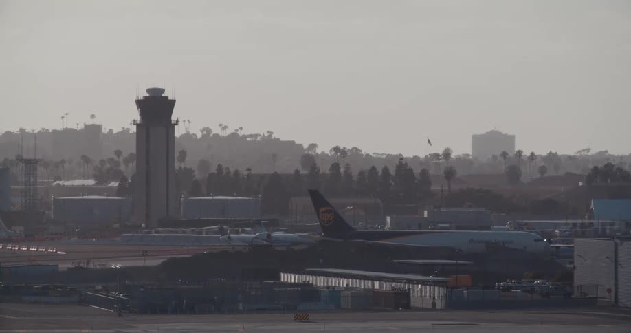 A hazy view of an airport tarmac featuring a parked UPS cargo plane and the air traffic control tower