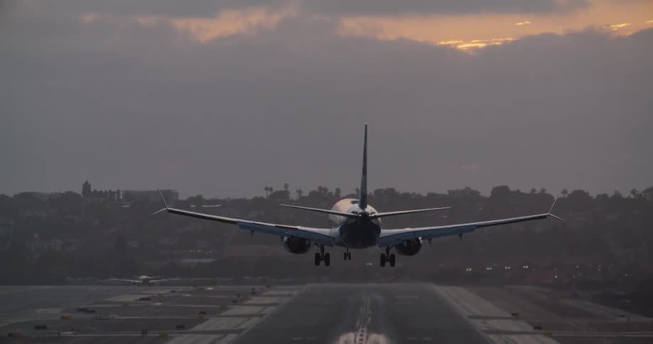 Rear view of a commercial airliner making a smooth landing on an airport runway at sunset in slow motion
