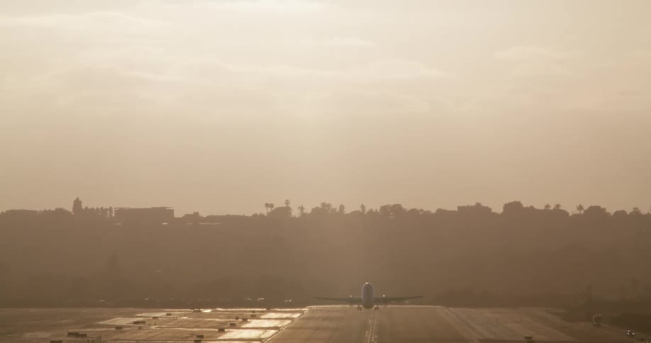 A commercial jet takes off in slow motion from an airport runway, silhouetted against a hazy golden hour sky