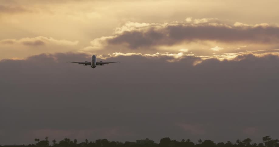 A passenger airplane takes off from a runway and ascends into a dramatic cloudy sky at sunset