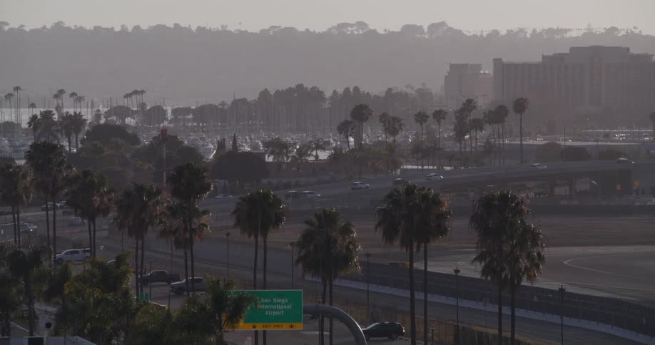 Hazy morning traffic moves along a highway lined with palm trees near the San Diego International Airport
