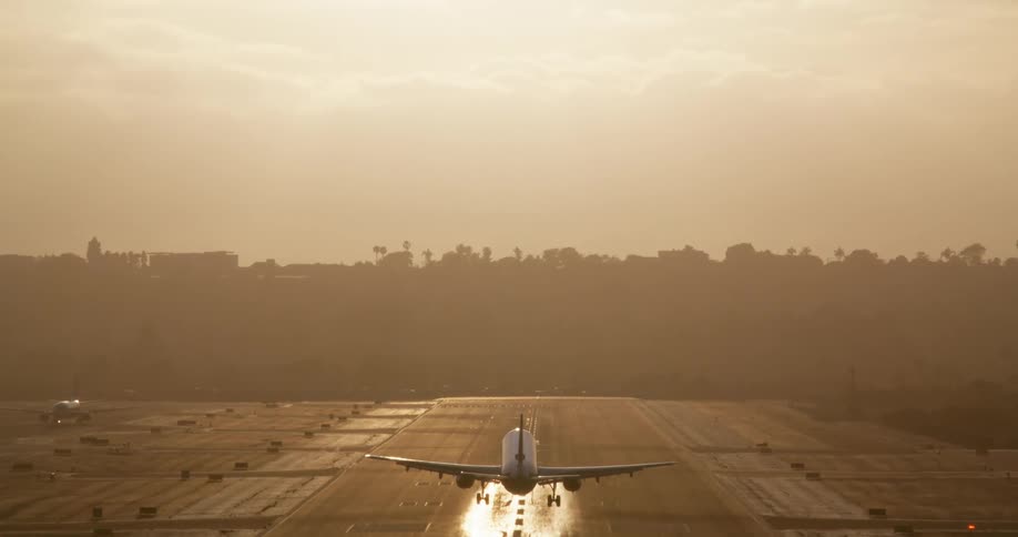 A passenger airplane is silhouetted against a golden sunset as it makes a dramatic slow-motion landing on a runway