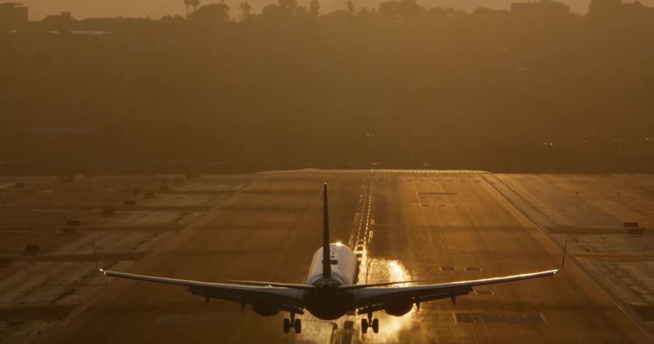 A commercial jet makes a dramatic landing on a runway, silhouetted against the golden light of a stunning sunset