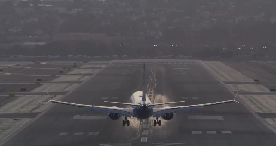Slow motion footage from behind a commercial airplane as it descends and lands on a runway at dusk