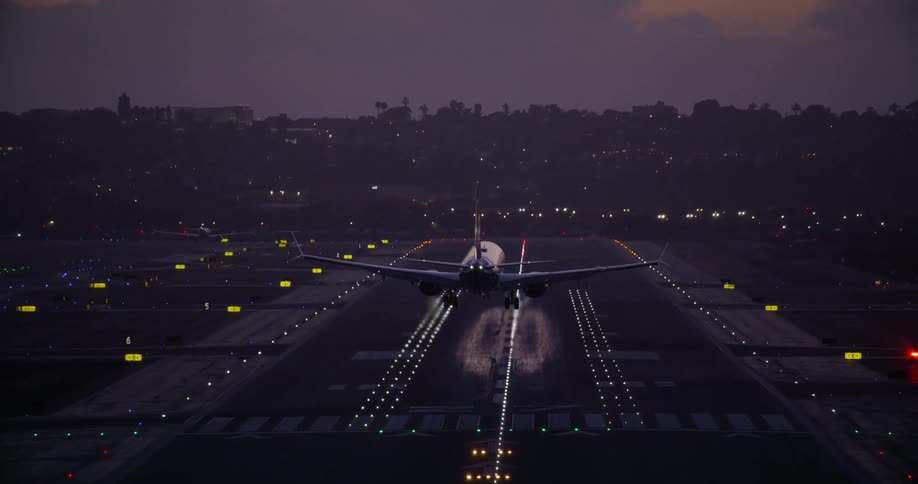 A commercial airplane with its landing lights on approaches and touches down on an airport runway against a twilight sky