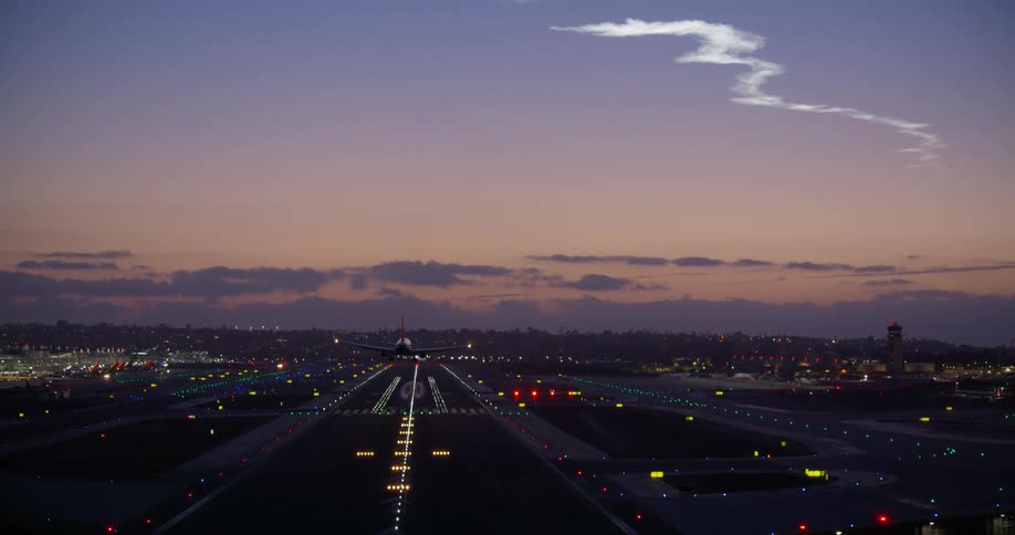A passenger jet makes a final approach and lands on an illuminated runway at twilight