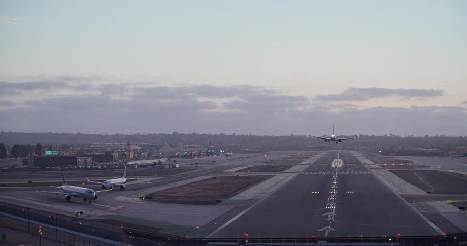 A commercial jetliner descends from a cloudy sky and lands smoothly on an illuminated airport runway at dusk