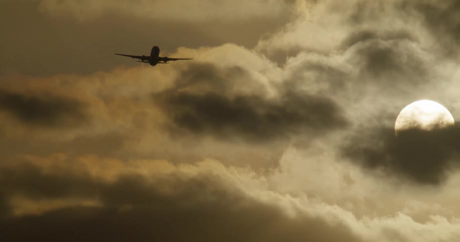A passenger airplane is silhouetted as it flies away into a dramatic, golden, cloudy sky towards the sun