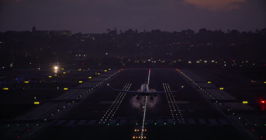 A commercial jetliner makes a final approach and lands on a brightly illuminated runway at dusk