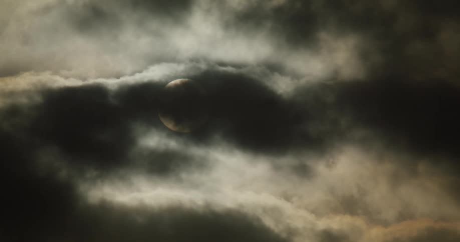 A silhouetted airplane flies past the sun which is obscured by dark and dramatic clouds