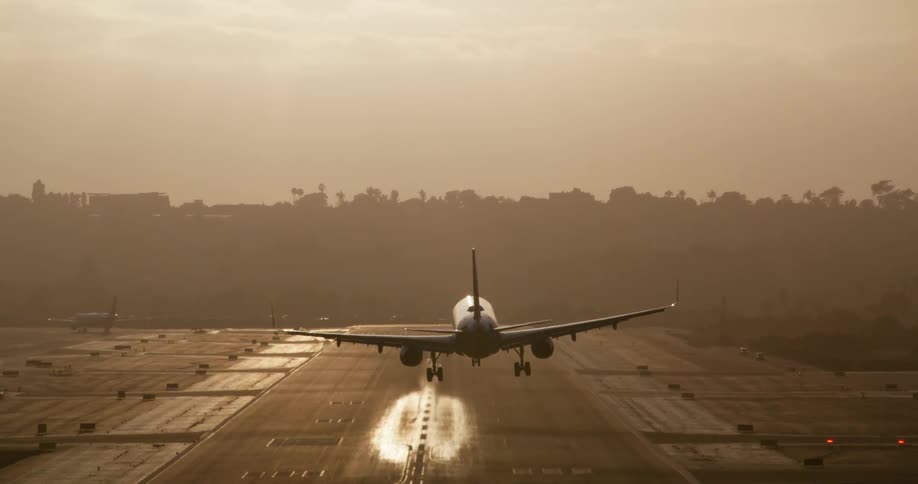 A passenger airplane is silhouetted against the bright sun as it makes a dramatic slow-motion landing on a runway