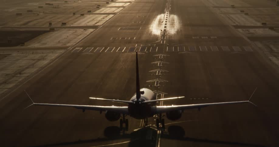 A slow-motion cinematic view from the tail of an airplane as it descends and touches down on the runway during a hazy golden hour