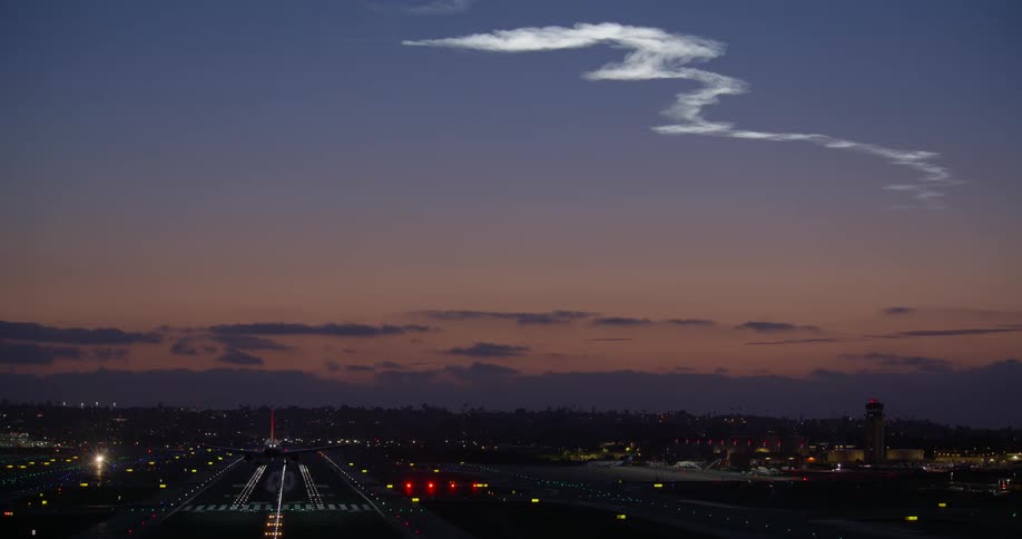A commercial airplane makes its final approach and lands on an illuminated airport runway at dusk
