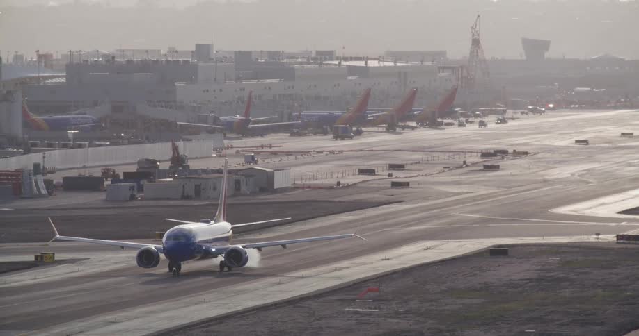 A passenger jet slowly taxis on the runway at a busy airport during a hazy day
