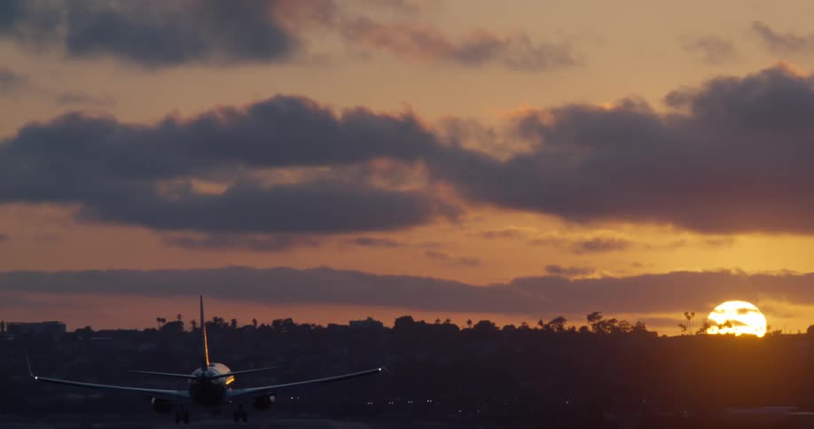 An airplane makes its final approach for landing, silhouetted against a dramatic and cloudy sunset sky
