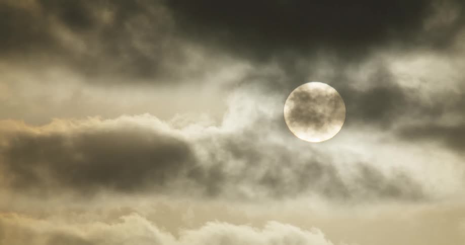 The bright sun is visible through a thick layer of dark, ominous clouds