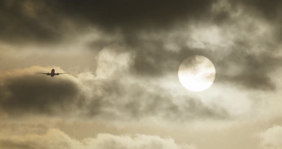 A silhouetted airplane takes off and flies away into a dramatic, sepia-toned sky with a bright sun behind the clouds