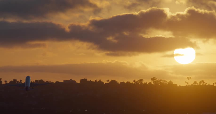 A silhouetted passenger jet takes off and ascends into a vibrant golden sky during a beautiful sunset