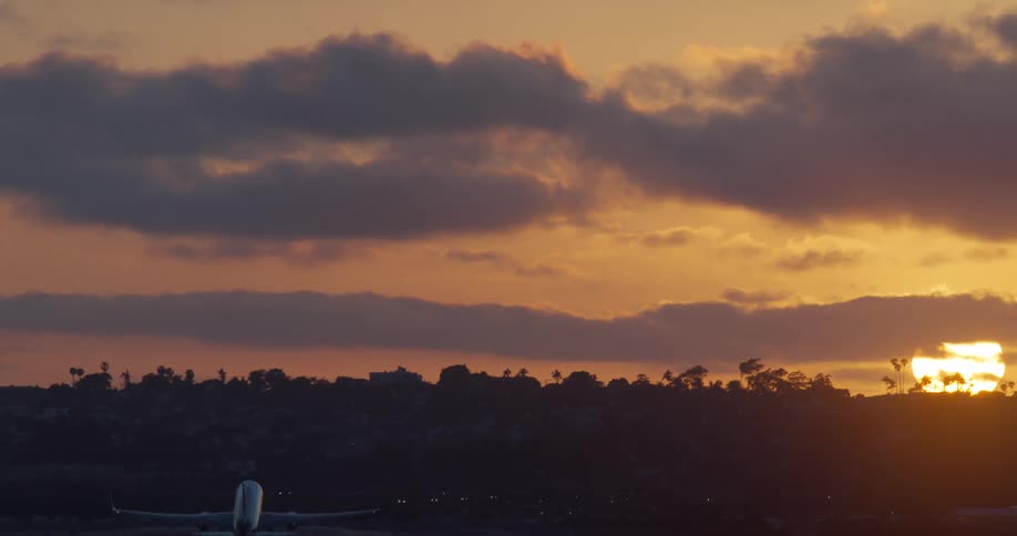 A passenger airplane takes off from a runway, silhouetted against a vibrant and cloudy sunset sky