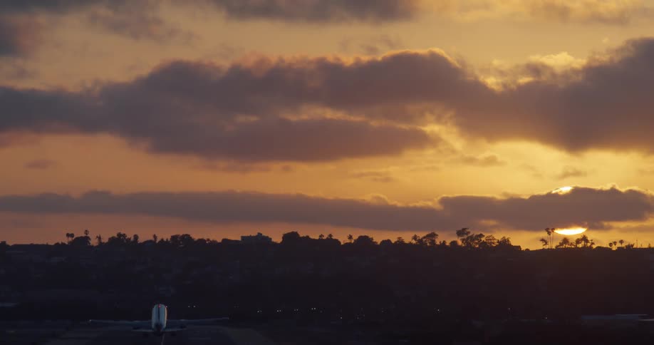 A silhouetted airplane takes off from a runway and flies into the beautiful orange sky at sunset