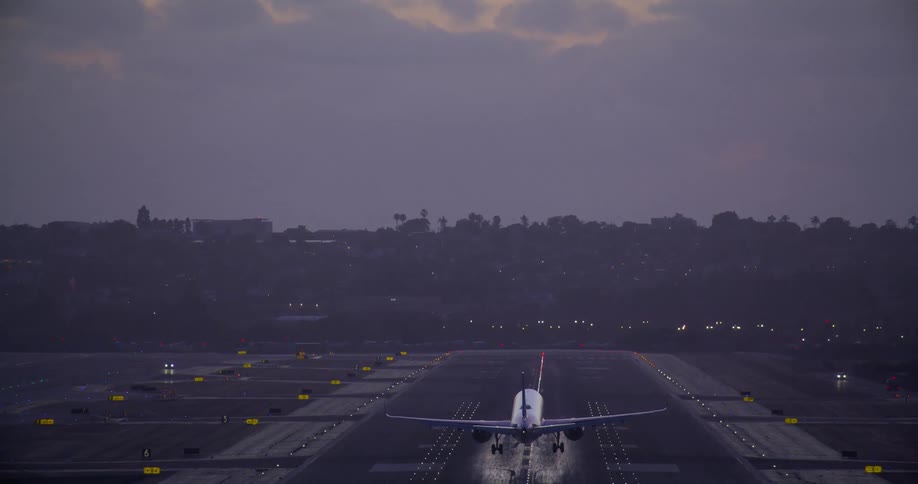 A passenger airplane makes its final approach and lands smoothly on an illuminated airport runway at dusk