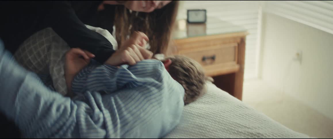 A mother playfully tickles her young son in his pajamas as he laughs in bed
