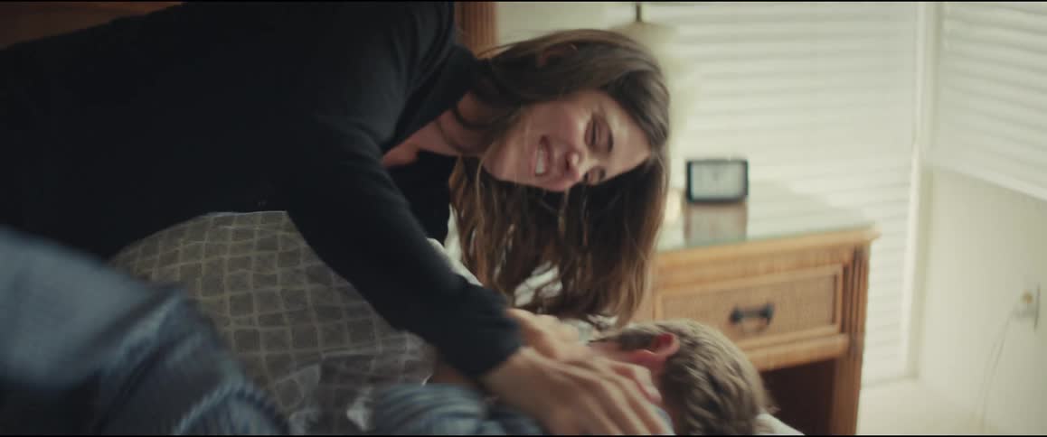 A mother playfully tickles her young son in his pajamas as he laughs in bed
