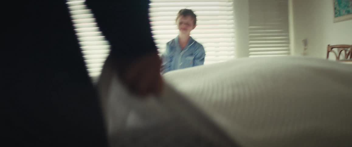 A happy boy in pajamas plays peek-a-boo with a parent on a sunlit bed