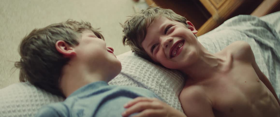 Two young brothers lie on pillows indoors smiling and laughing together in a cozy bedroom