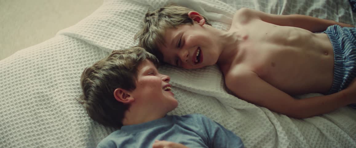 Two young brothers lying on a bed smiling and laughing together in soft morning light