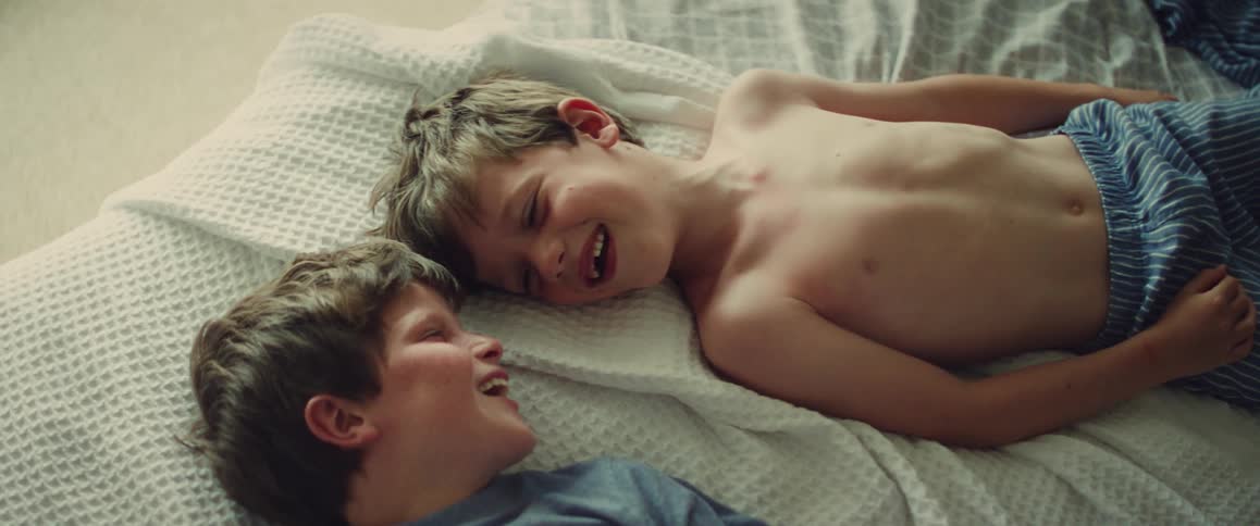 Two young brothers lying on a bed smiling and laughing together in soft morning light