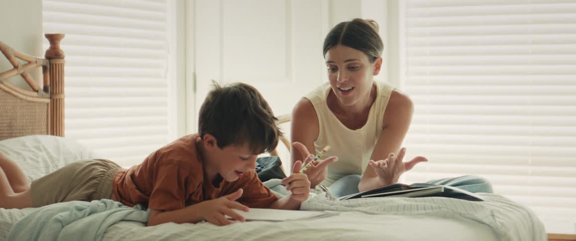 A caring mother helps her young son with his homework, patiently teaching him to count as they sit together on a sunlit bed