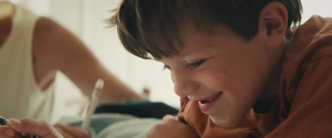 A close-up slow-motion shot of a happy young boy smiling while concentrating on his drawing