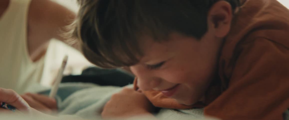 A close-up slow-motion shot of a happy young boy smiling while concentrating on his drawing