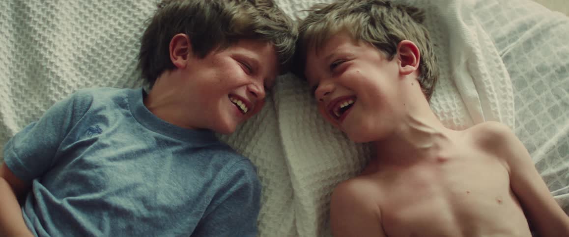 A close-up top-down view of two young brothers lying in bed, making funny faces and laughing together