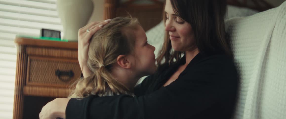 An affectionate mother cuddles with her young daughter, sharing tender kisses and smiles in a cozy bedroom